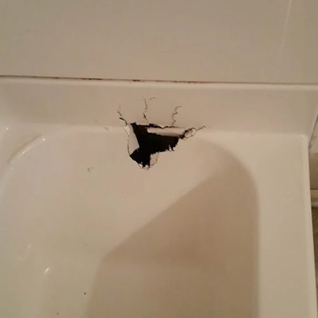 Close up of a large crack spreading across a white fiberglass bathtub surface